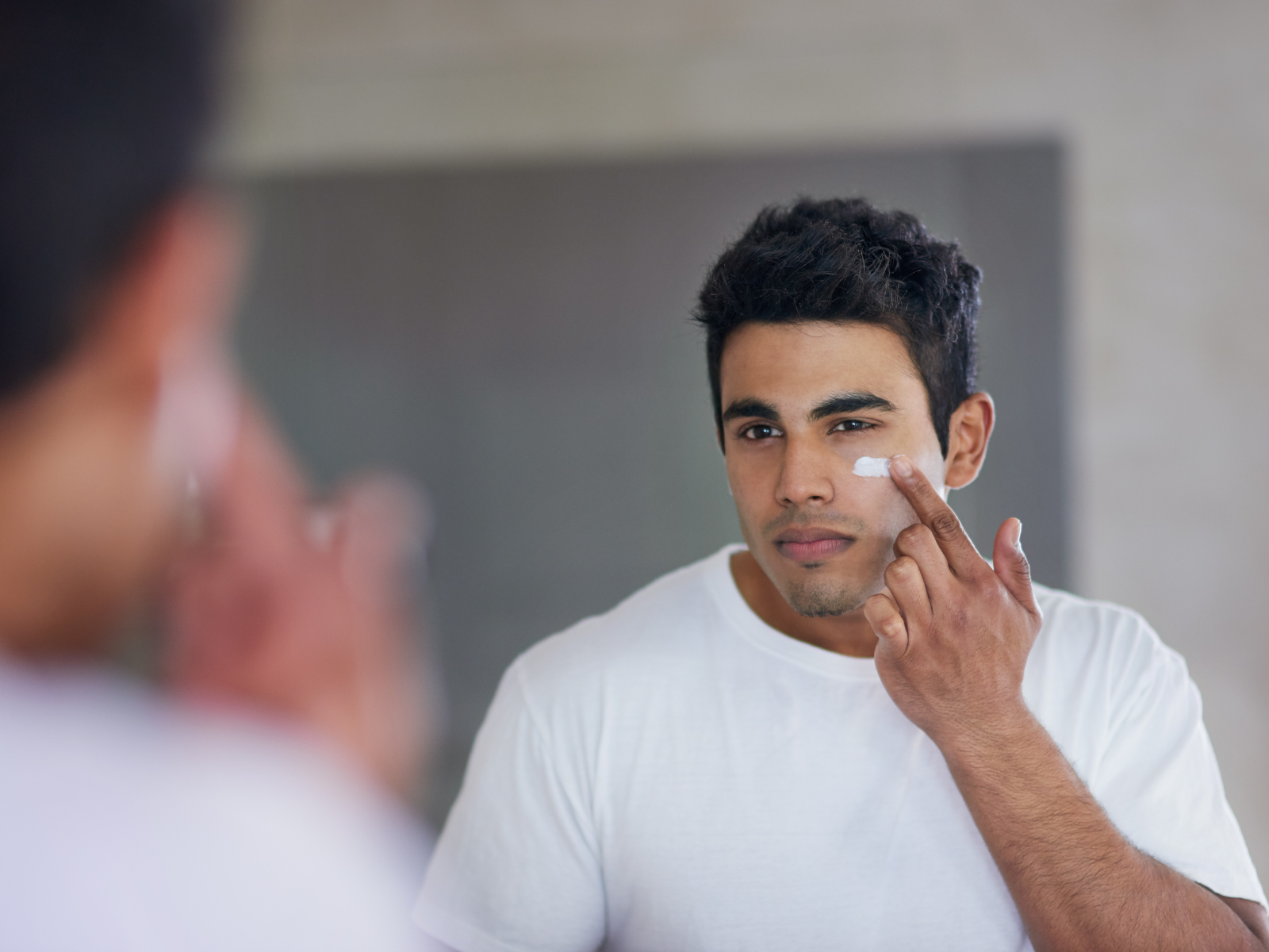 Mens skin care and skin cream being applied by a male in front of a mirror